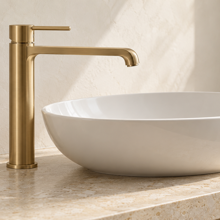 Tall brushed brass basin mixer beside a white above-counter basin, showing spout reach and clearance above the rim.